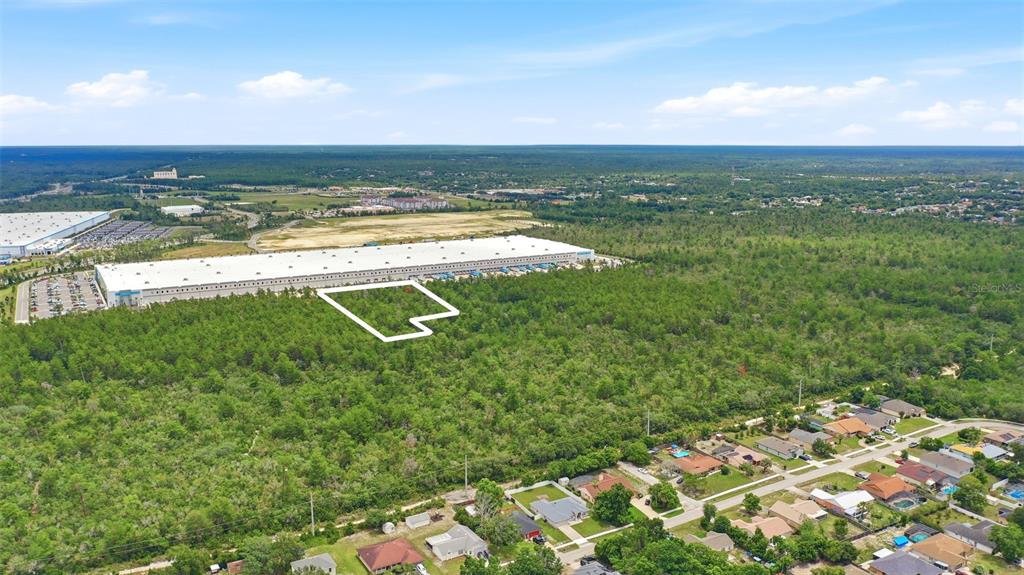 An aerial view shows a large warehouse facility situated behind a residential neighborhood and forest — AMELIA (PAPER) AVENUE, DELTONA, FL