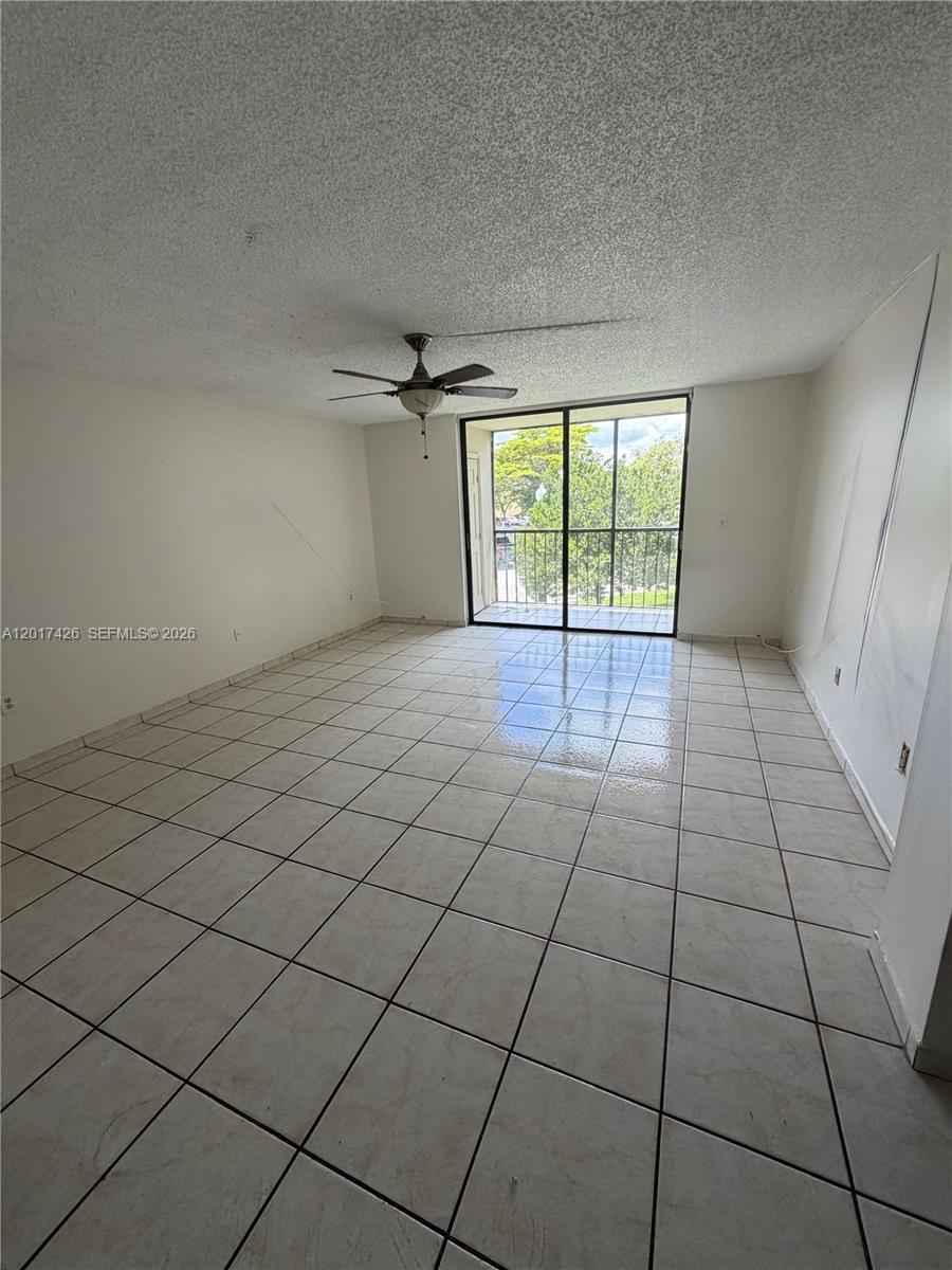An empty living room features white tiled floors, a ceiling fan, and a sliding glass door — 8035 SW 107th Ave # 203, Miami FL 33173, MIAMI, FL