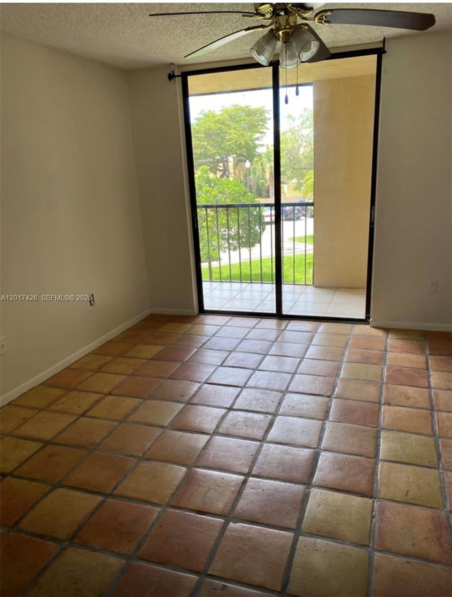An empty room features terracotta tile flooring, a ceiling fan, and sliding glass balcony doors — 8035 SW 107th Ave # 203, Miami FL 33173, MIAMI, FL