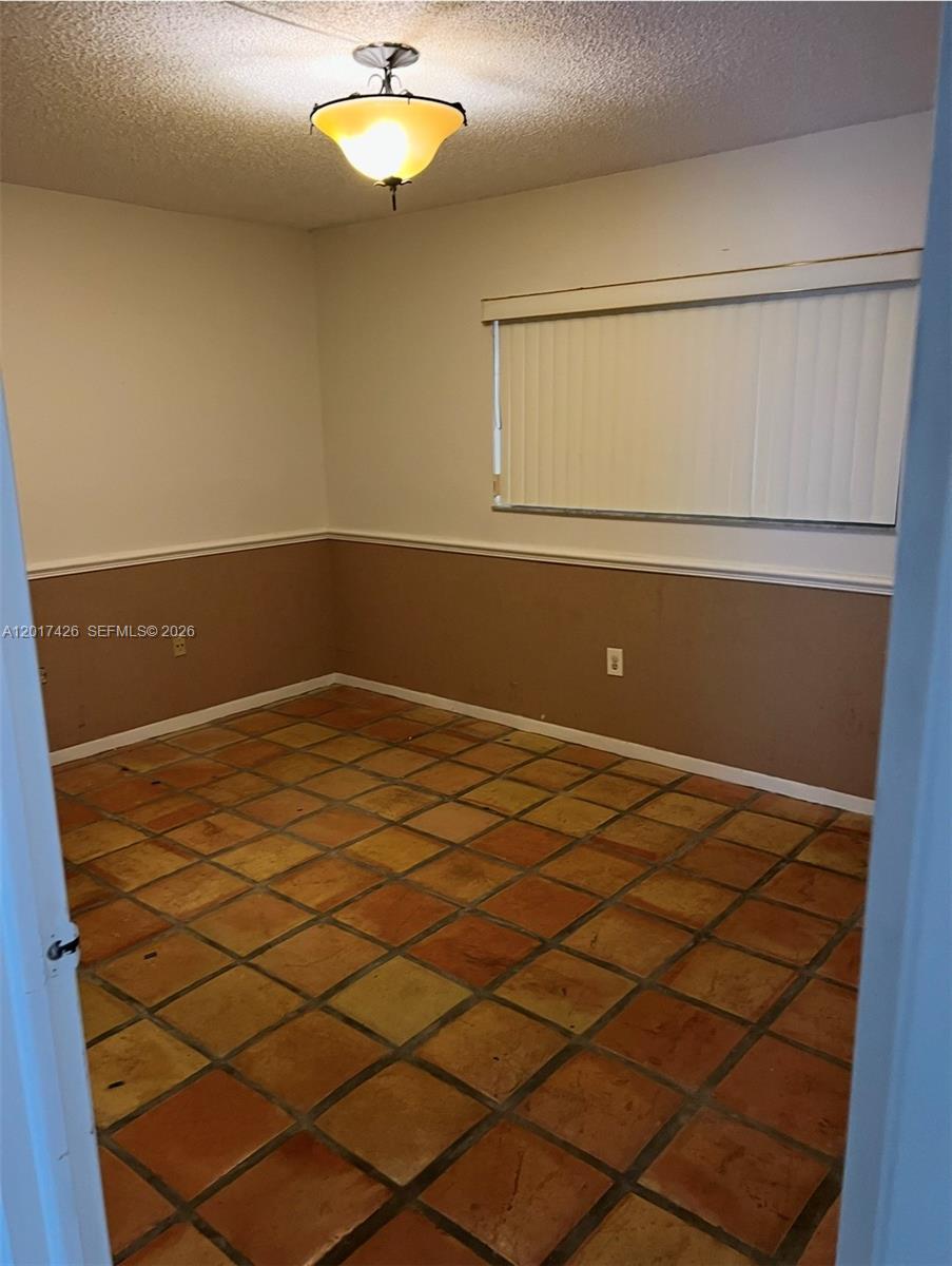 An empty room features terracotta tile flooring, two-toned walls with chair rail molding, and a window — 8035 SW 107th Ave # 203, Miami FL 33173, MIAMI, FL