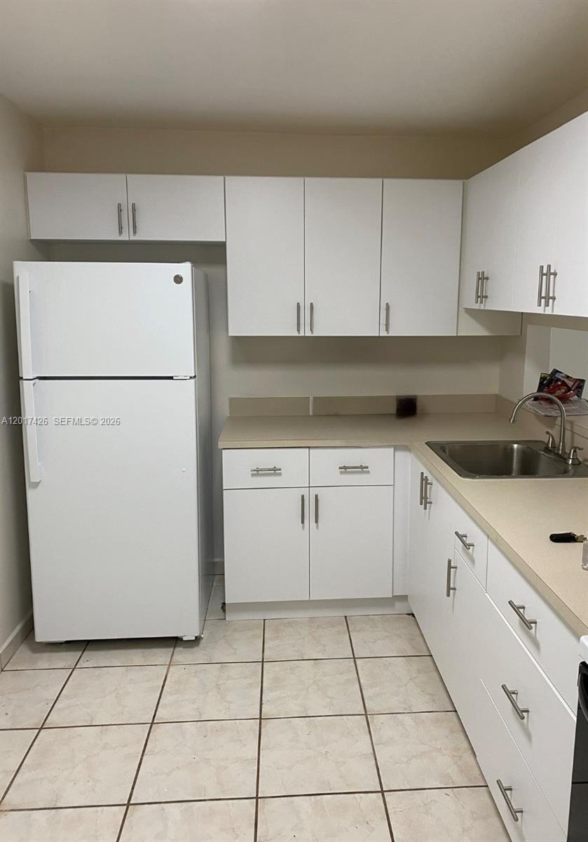 A kitchen features white cabinets, a white refrigerator, and beige countertops over tiled floors — 8035 SW 107th Ave # 203, Miami FL 33173, MIAMI, FL