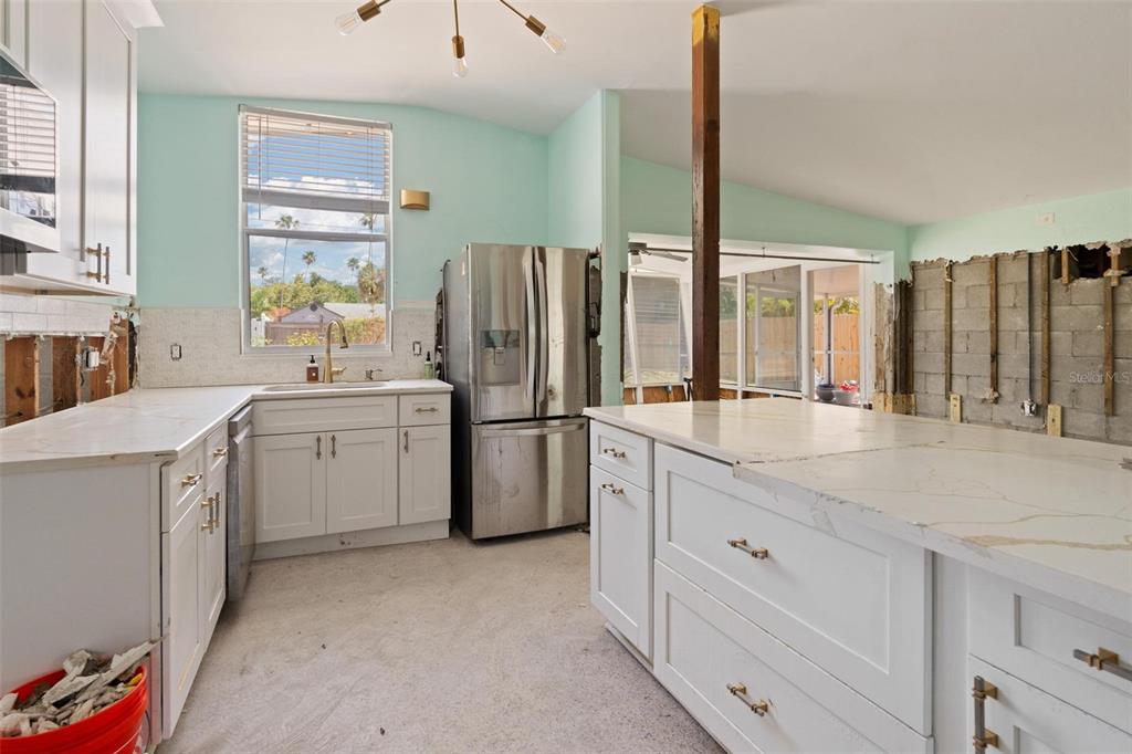 An unfinished kitchen features white cabinets, a large island, stainless steel appliances, and exposed walls — 3727 ALABAMA AVENUE NE, ST PETERSBURG, FL