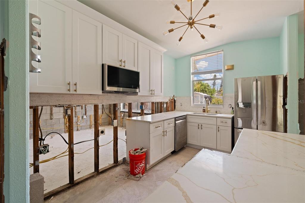 A kitchen under renovation features white cabinets, stainless steel appliances, and exposed wall studs — 3727 ALABAMA AVENUE NE, ST PETERSBURG, FL