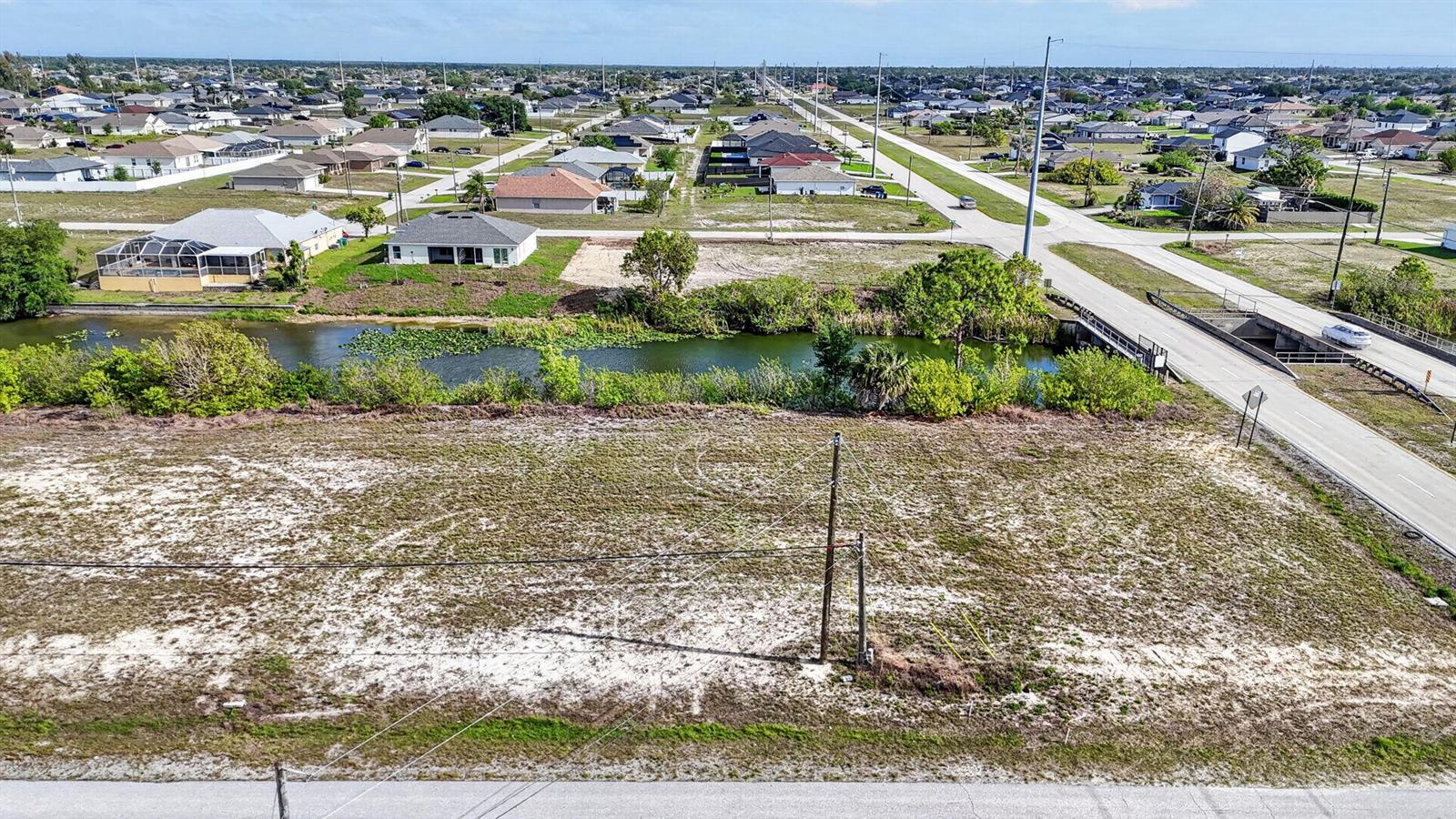 An aerial view shows a vacant lot bordering a canal next to a paved road — 5 NW 19th Terrace, Cape Coral FL 33993, CAPE CORAL, FL