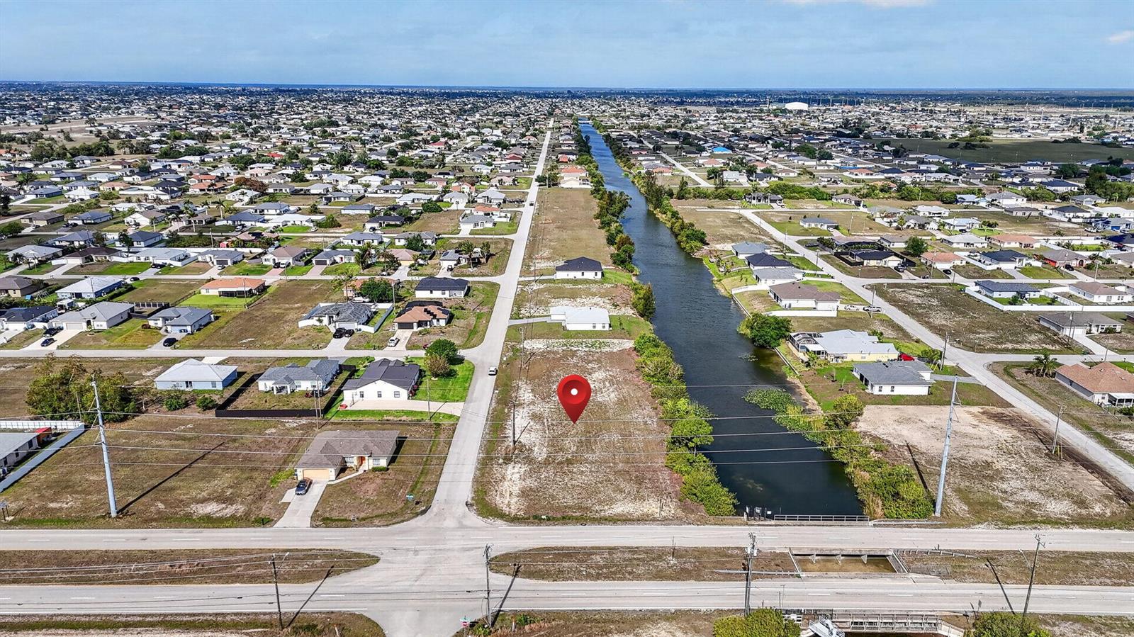 An aerial view shows a vacant residential lot situated between a road and a canal — 5 NW 19th Terrace, Cape Coral FL 33993, CAPE CORAL, FL