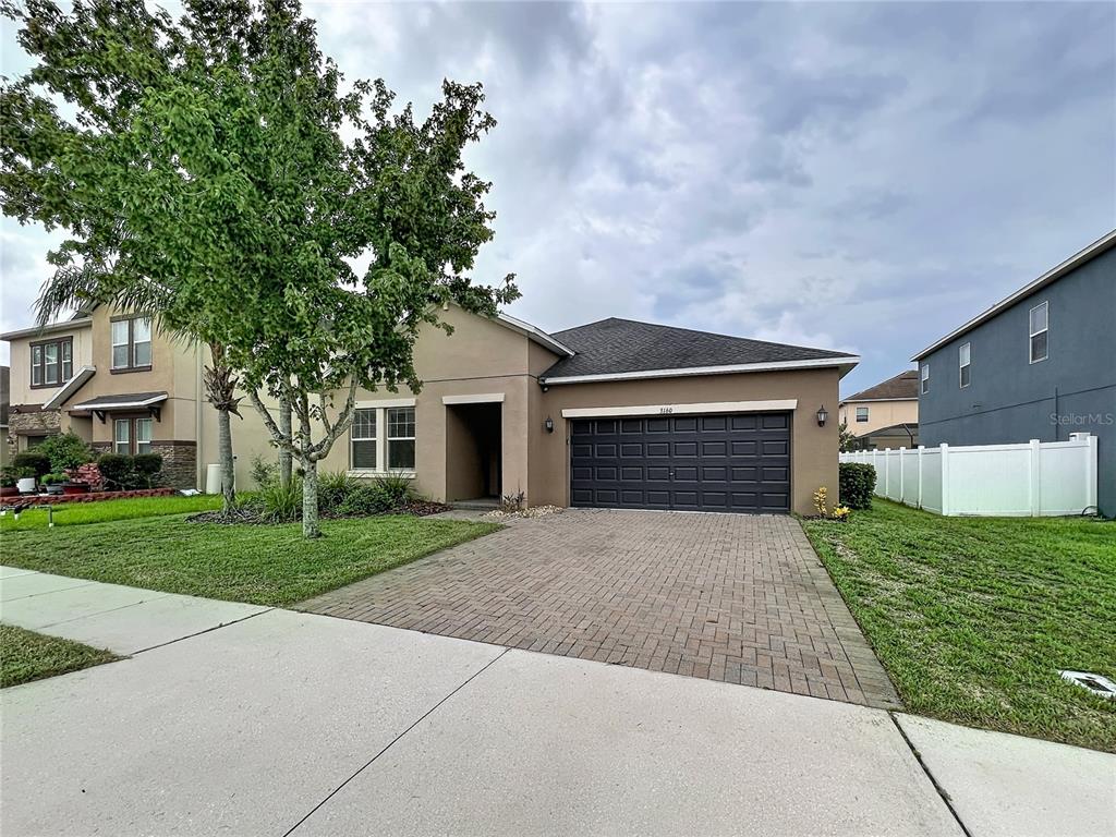 A single-story house with a tan stucco exterior, a dark garage door, and a paved driveway — 3160 CALVANO DRIVE, LAND O LAKES, FL