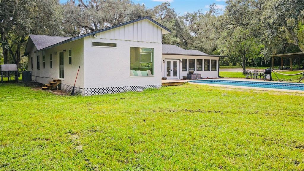 A white house with a swimming pool sits on a grassy lawn surrounded by trees — 10245 E TRAILS END ROAD, FLORAL CITY, FL