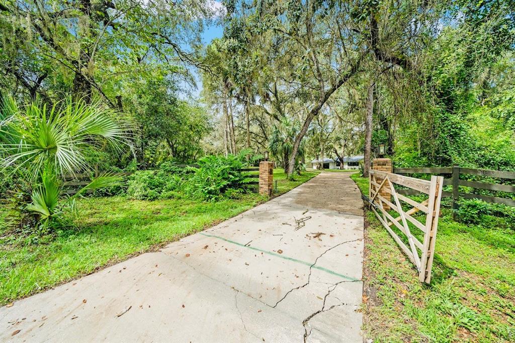 A concrete driveway leads through a wooden gate toward a house surrounded by mature trees — 10245 E TRAILS END ROAD, FLORAL CITY, FL