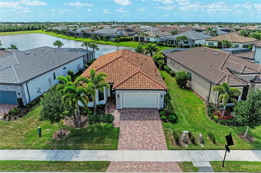 An aerial view shows a suburban house with a tiled roof and brick paver driveway — 7412 SUMMERLAND COVE, LAKEWOOD RANCH, FL