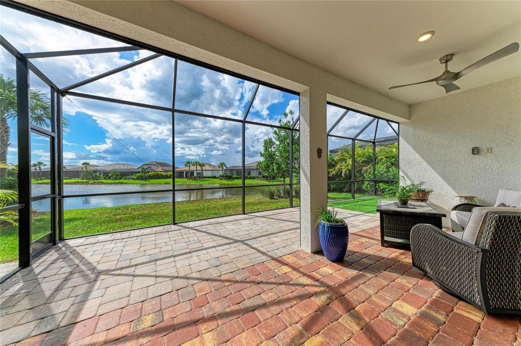 A screened-in patio with brick pavers overlooks a pond and neighboring houses — 7412 SUMMERLAND COVE, LAKEWOOD RANCH, FL