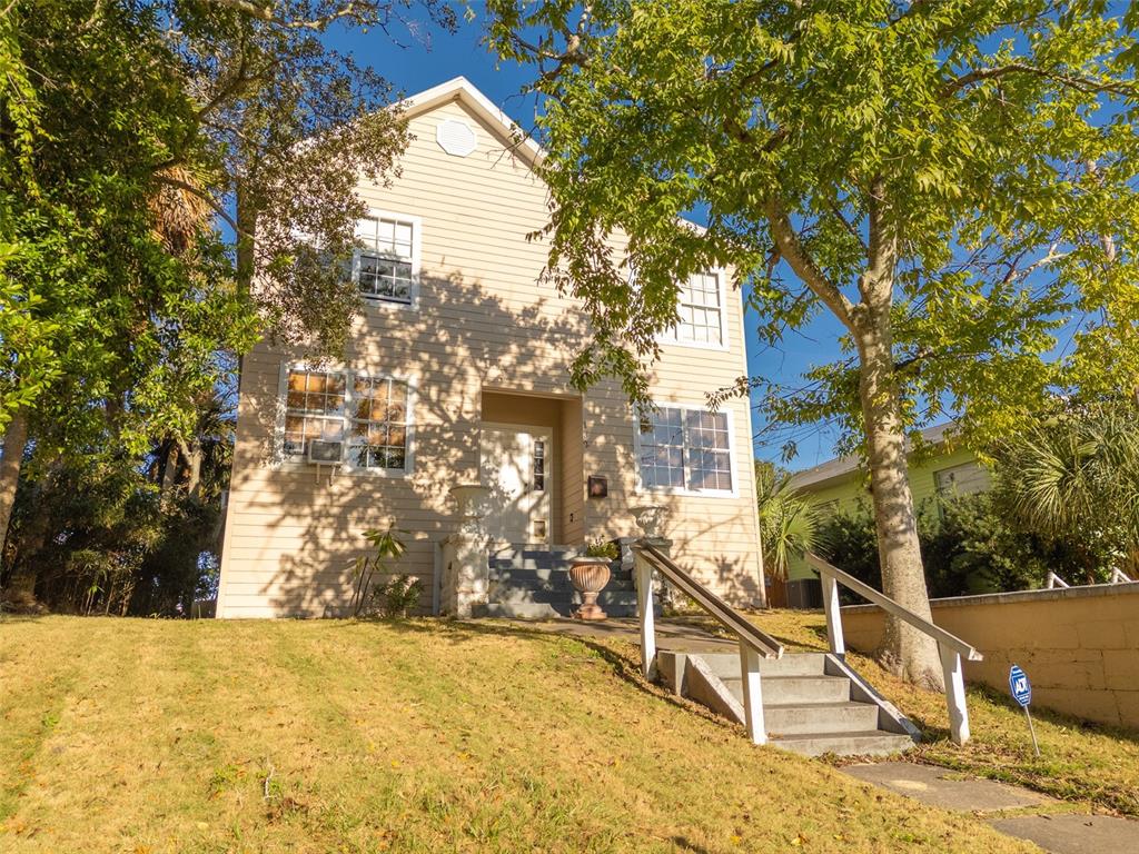 A two-story beige house with a front staircase sits on a grassy, sloped lot — 132 N PENINSULA DRIVE, DAYTONA BEACH, FL