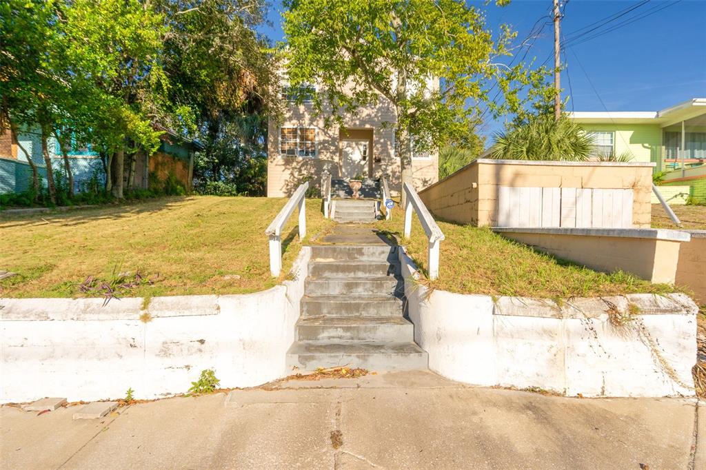 A concrete staircase with white railings leads up a grassy hill to a house exterior — 132 N PENINSULA DRIVE, DAYTONA BEACH, FL