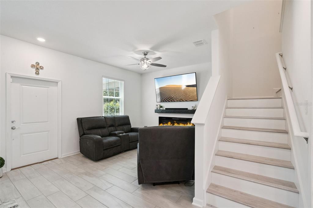 A living room features a fireplace, a wall-mounted television, gray seating, and a staircase — 15755 WATER SPRING BOULEVARD, WINTER GARDEN, FL