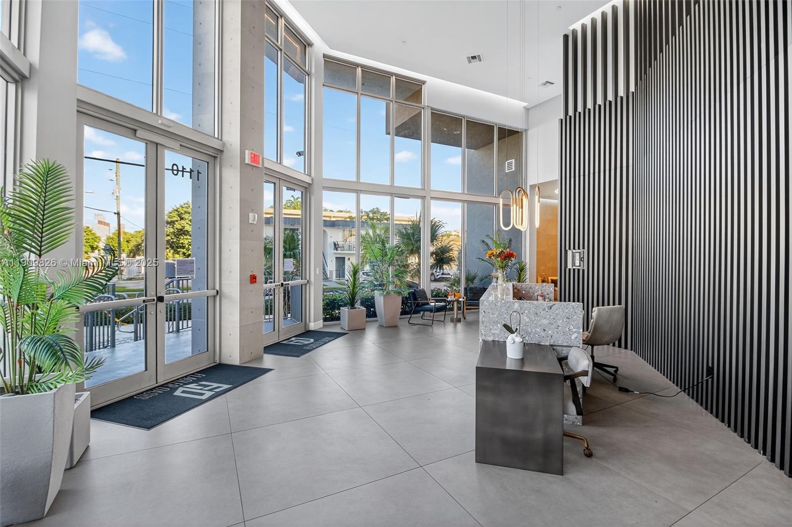 A modern lobby features floor-to-ceiling windows, a stone reception desk, and vertical wall slats — 1110 NW 1 ST # 502, Miami FL 33128, MIAMI, FL