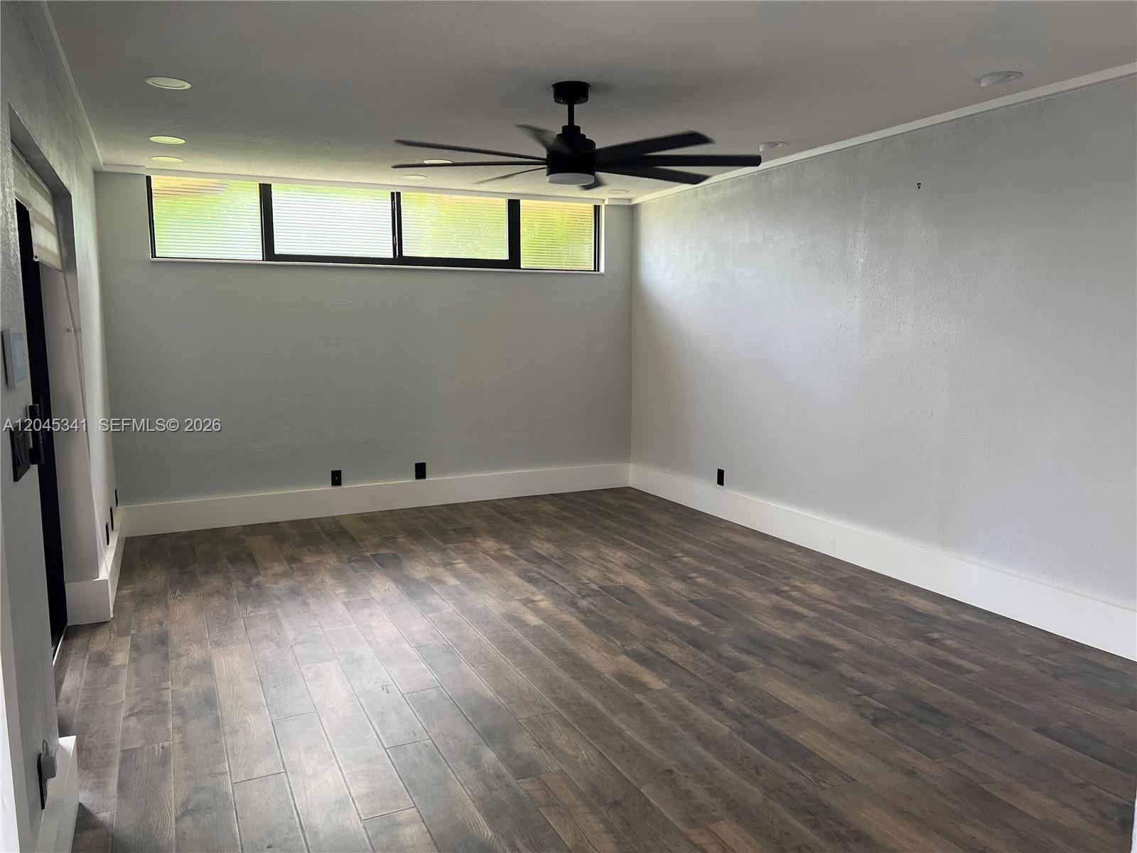 An empty room features gray walls, dark wood-look flooring, and a modern ceiling fan — 3940 Victoria Dr, West Palm Beach FL 33406, WEST PALM BEACH, FL