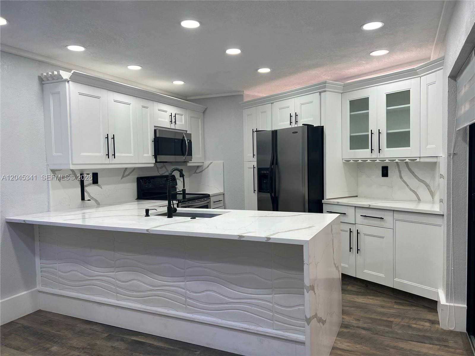 A modern kitchen features white cabinetry, marble-patterned countertops, a waterfall island, and stainless steel appliances — 3940 Victoria Dr, West Palm Beach FL 33406, WEST PALM BEACH, FL