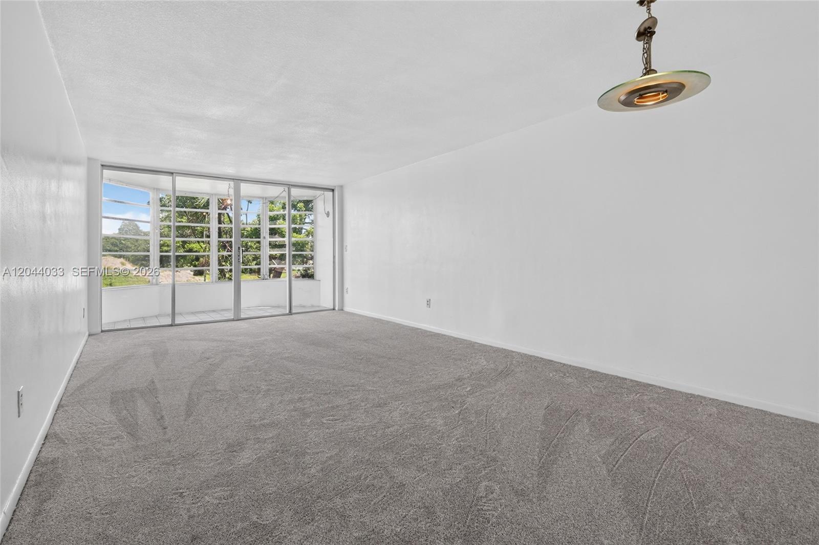 An empty room features gray carpeting, white walls, and a sliding glass door to a balcony — 1501 NE 191st St # C203, Miami FL 33179, MIAMI, FL