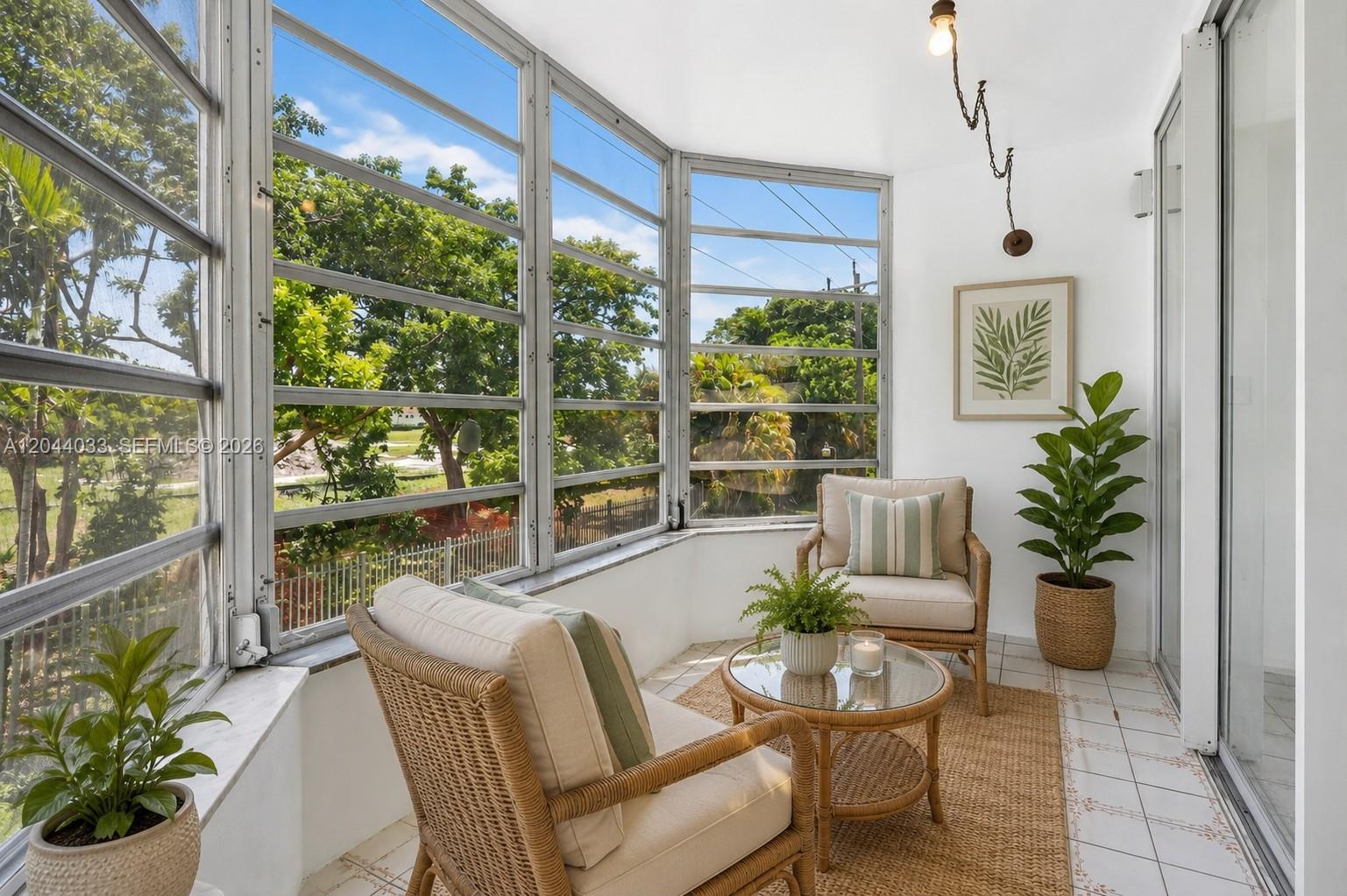 A sunroom features wicker chairs, a glass coffee table, and large windows overlooking trees — 1501 NE 191st St # C203, Miami FL 33179, MIAMI, FL