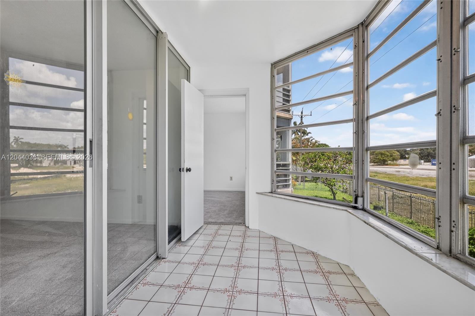 A sunroom with tiled flooring, large windows, and a doorway leading into a carpeted room — 1501 NE 191st St # C203, Miami FL 33179, MIAMI, FL
