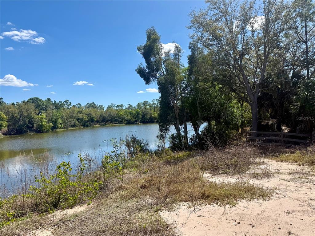 A view of a lake from a sandy, grassy bank with trees and a fence — 13212 & 13206 MARYLAND AVENUE, PUNTA GORDA, FL