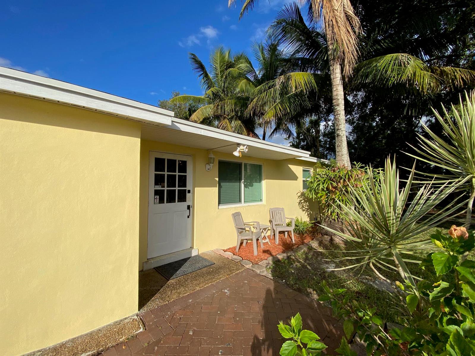 A yellow exterior wall features a white door, a window, and two chairs on a patio — 9015 Twig Road, Lake Worth FL 33467, LAKE WORTH, FL