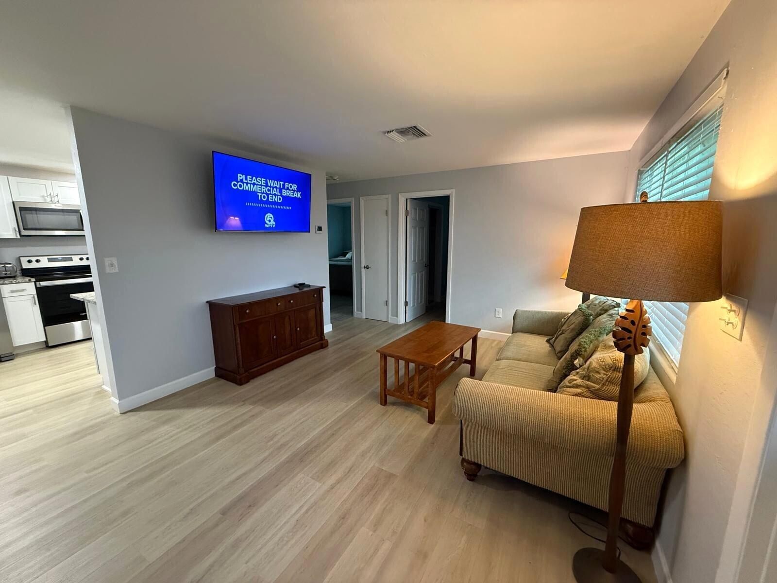 A living room with light wood flooring, a sofa, a coffee table, and a wall-mounted television — 9015 Twig Road, Lake Worth FL 33467, LAKE WORTH, FL
