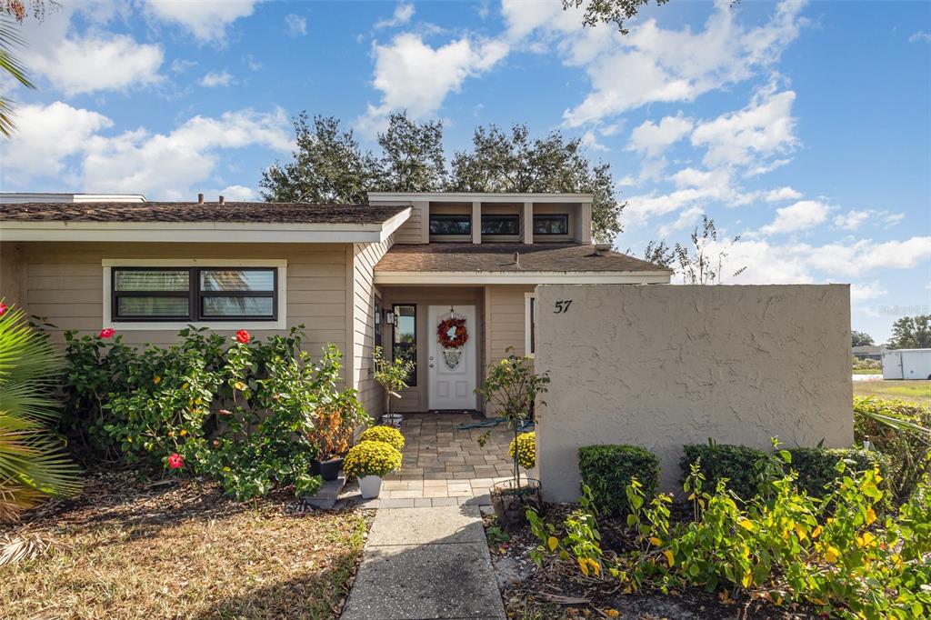 A tan house exterior features a paved walkway, a front door with a wreath, and landscaping — 5225 IMPERIAL LAKES BOULEVARD UNIT 57, MULBERRY, FL