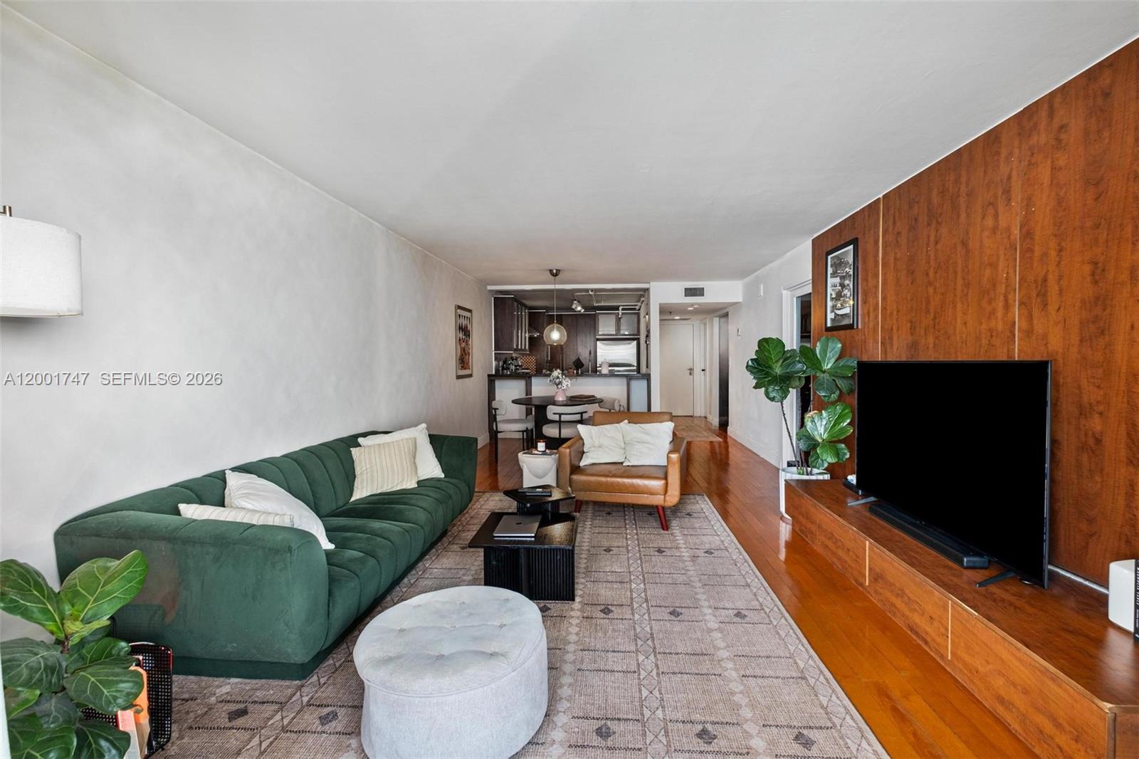 A living room features a green sofa, a leather armchair, and a wood-paneled media wall — 555 NE 15th St # 26F, Miami FL 33132, MIAMI, FL