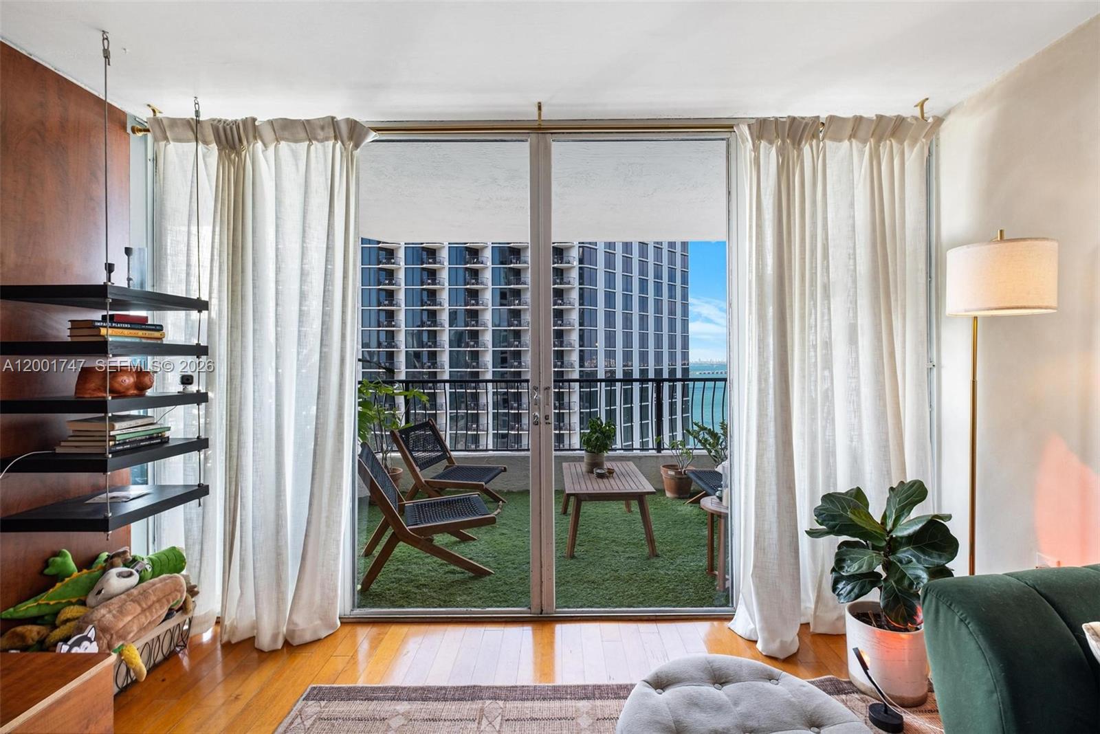 A living room features hardwood floors, a balcony with artificial turf, and floor-to-ceiling glass doors — 555 NE 15th St # 26F, Miami FL 33132, MIAMI, FL