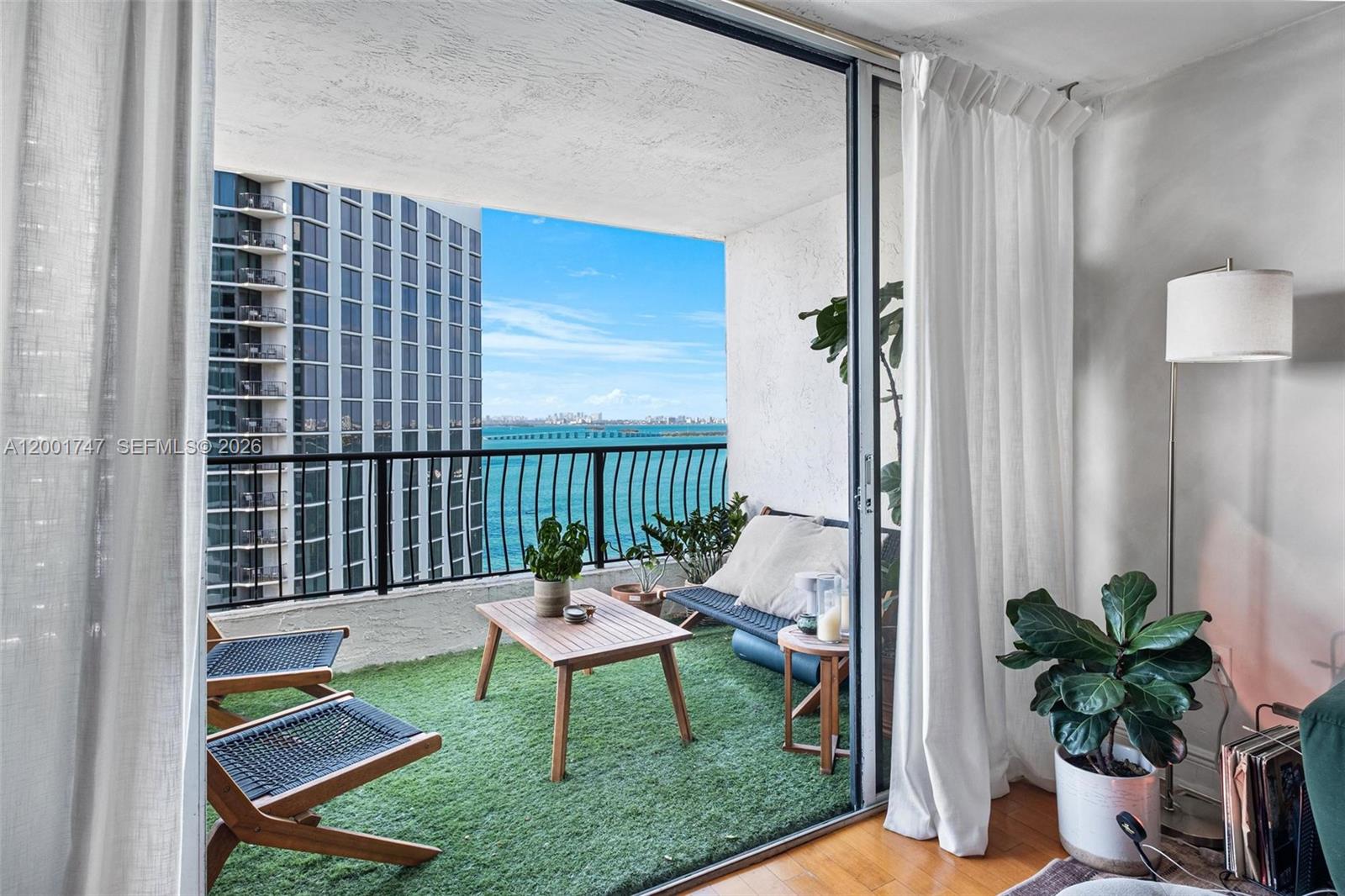 A balcony with artificial turf, outdoor furniture, and a view of the ocean and buildings — 555 NE 15th St # 26F, Miami FL 33132, MIAMI, FL