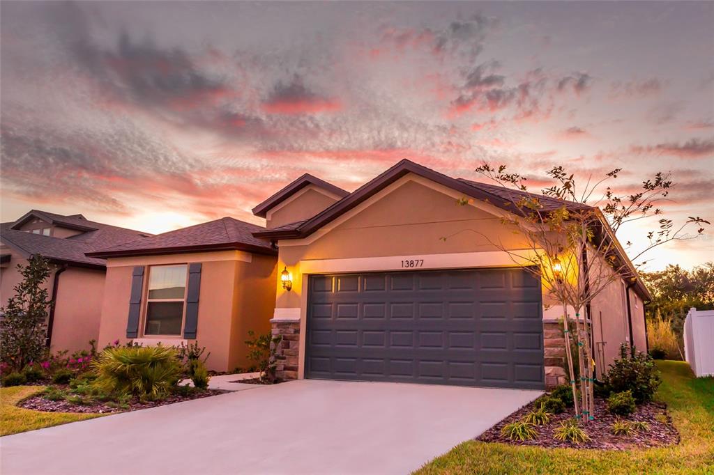 A single-story house with a two-car garage and stone accents at sunset — 13877 CARLOW PARK DRIVE, RIVERVIEW, FL