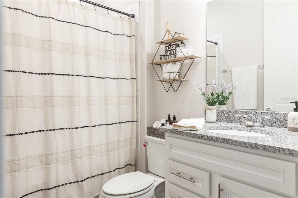 A bathroom features a granite vanity, white cabinetry, a shower curtain, and wall-mounted shelving — 13877 CARLOW PARK DRIVE, RIVERVIEW, FL