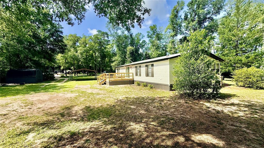 A single-story manufactured home with a wooden deck sits on a grassy, wooded lot — 7350 SE 78TH PLACE, TRENTON, FL