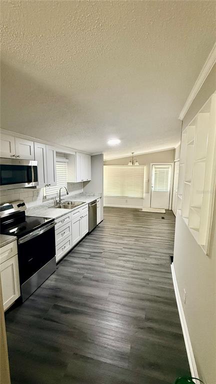 A kitchen with white cabinets, stainless steel appliances, and wood-look flooring leads to a dining area — 7350 SE 78TH PLACE, TRENTON, FL