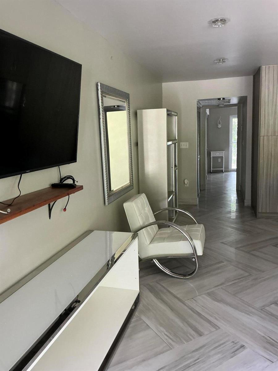 A room features a white chair, a wall-mounted television, and light-colored wood-look tile flooring — 40 Ventnor Drive, Deerfield Beach FL 33442, DEERFIELD BEACH, FL