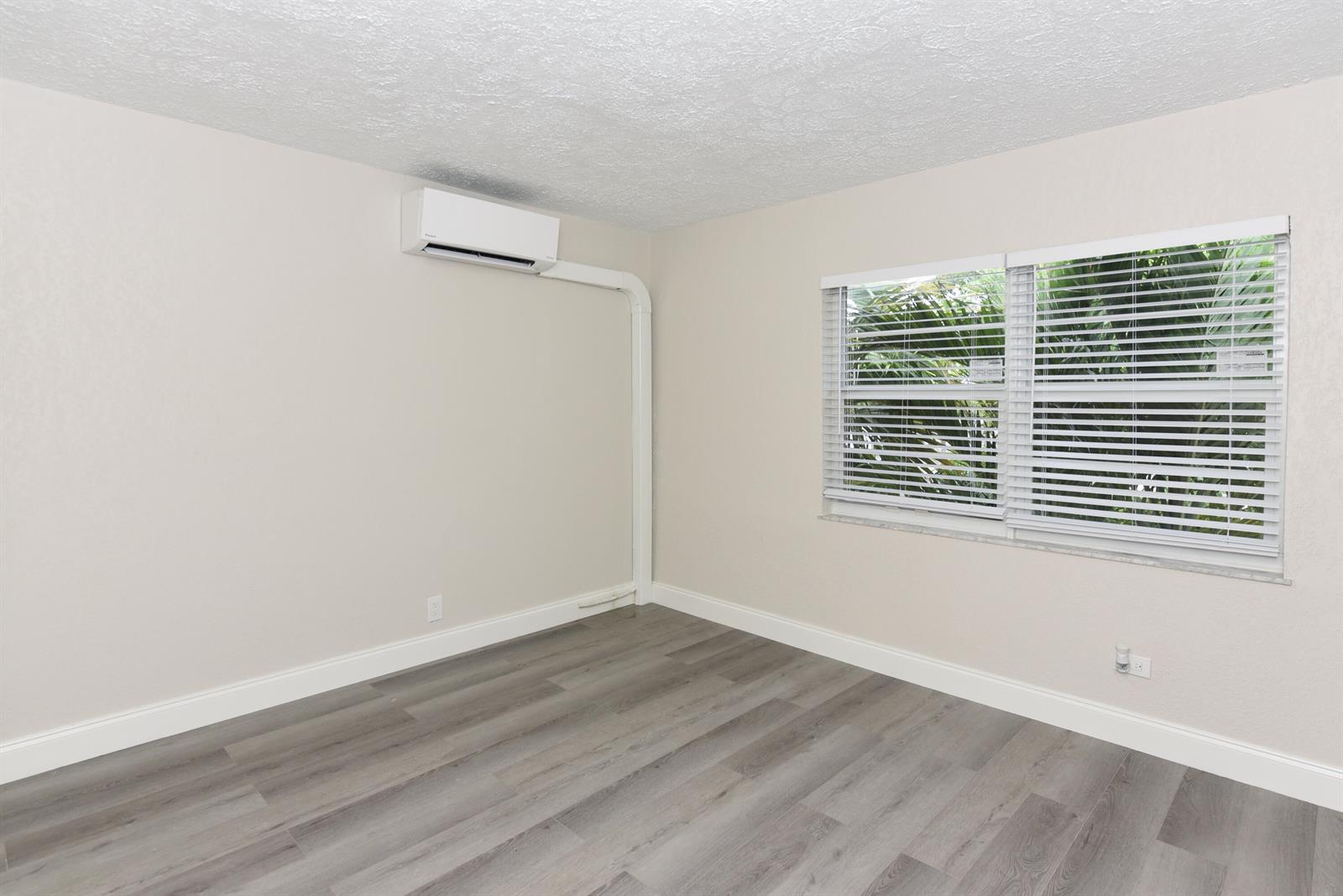 An empty room features light walls, wood-look flooring, a wall-mounted air conditioner, and white blinds — 605 N Federal Highway # 7, FL 33460, FL