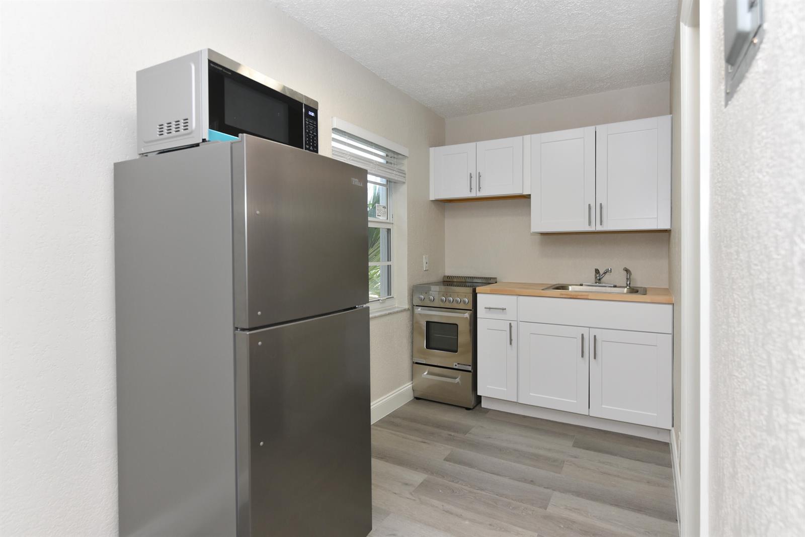 A small kitchen features white cabinets, stainless steel appliances, and wood-look flooring — 605 N Federal Highway # 7, FL 33460, FL