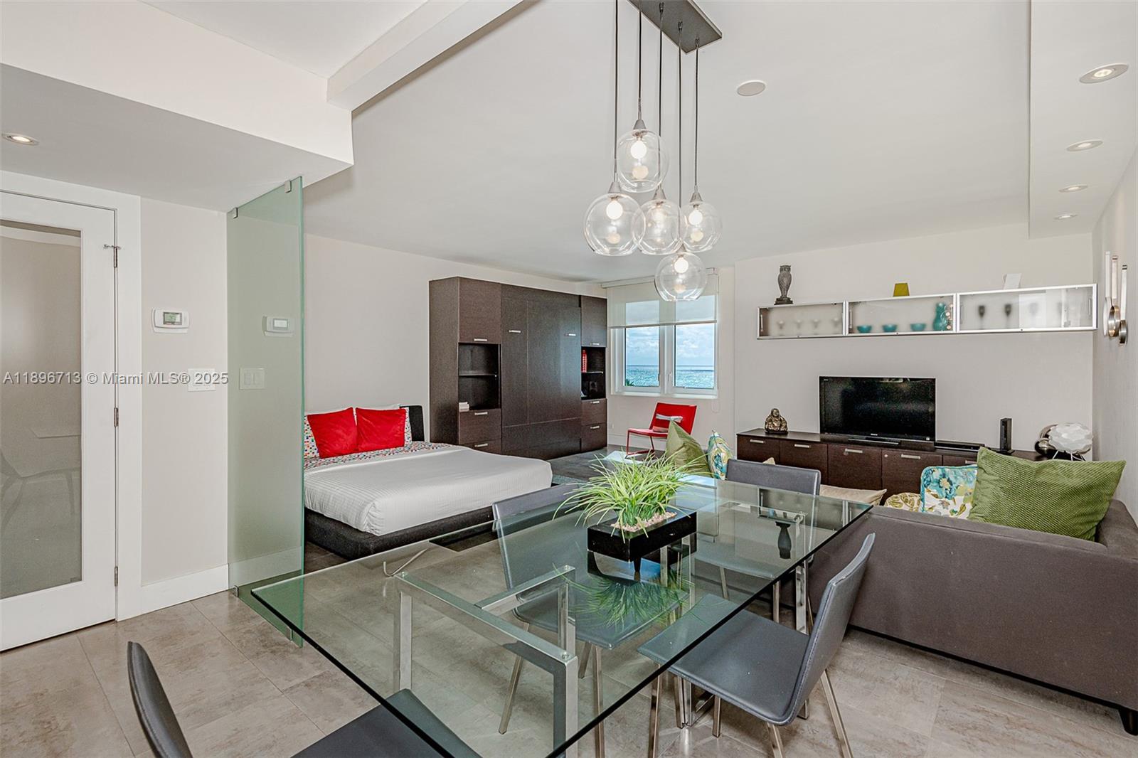 A studio apartment features a glass-topped dining table, a bed, and a view of the ocean — 2301 Collins Ave # 723, Miami Beach FL 33139, MIAMI BEACH, FL