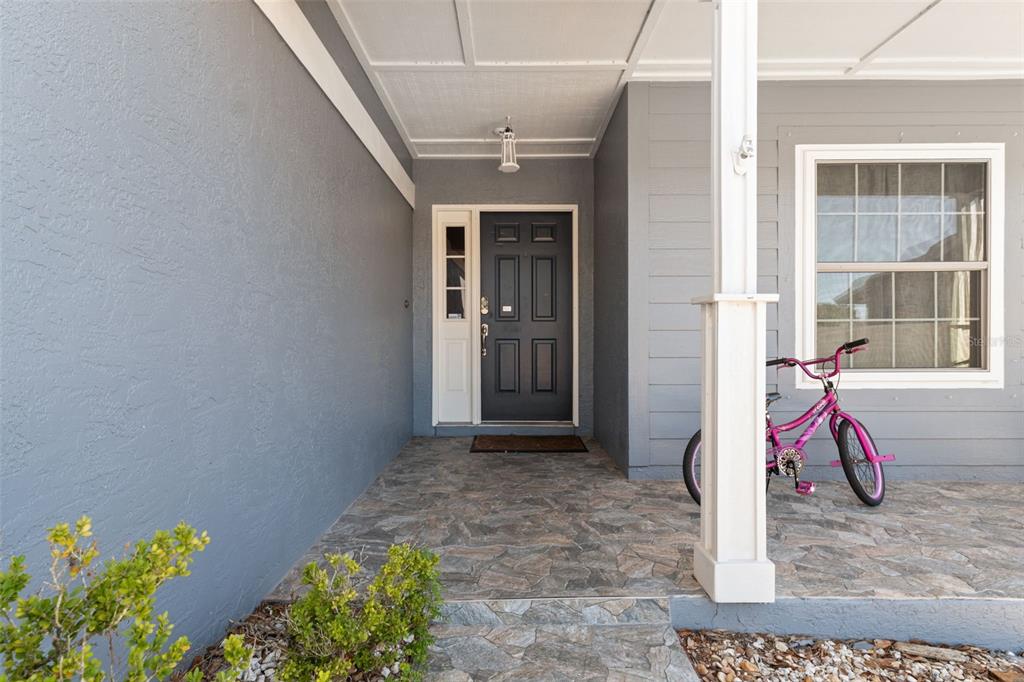 A covered front porch with stone flooring, a dark door, and a pink bicycle — 24138 TWIN COURT, LAND O LAKES, FL
