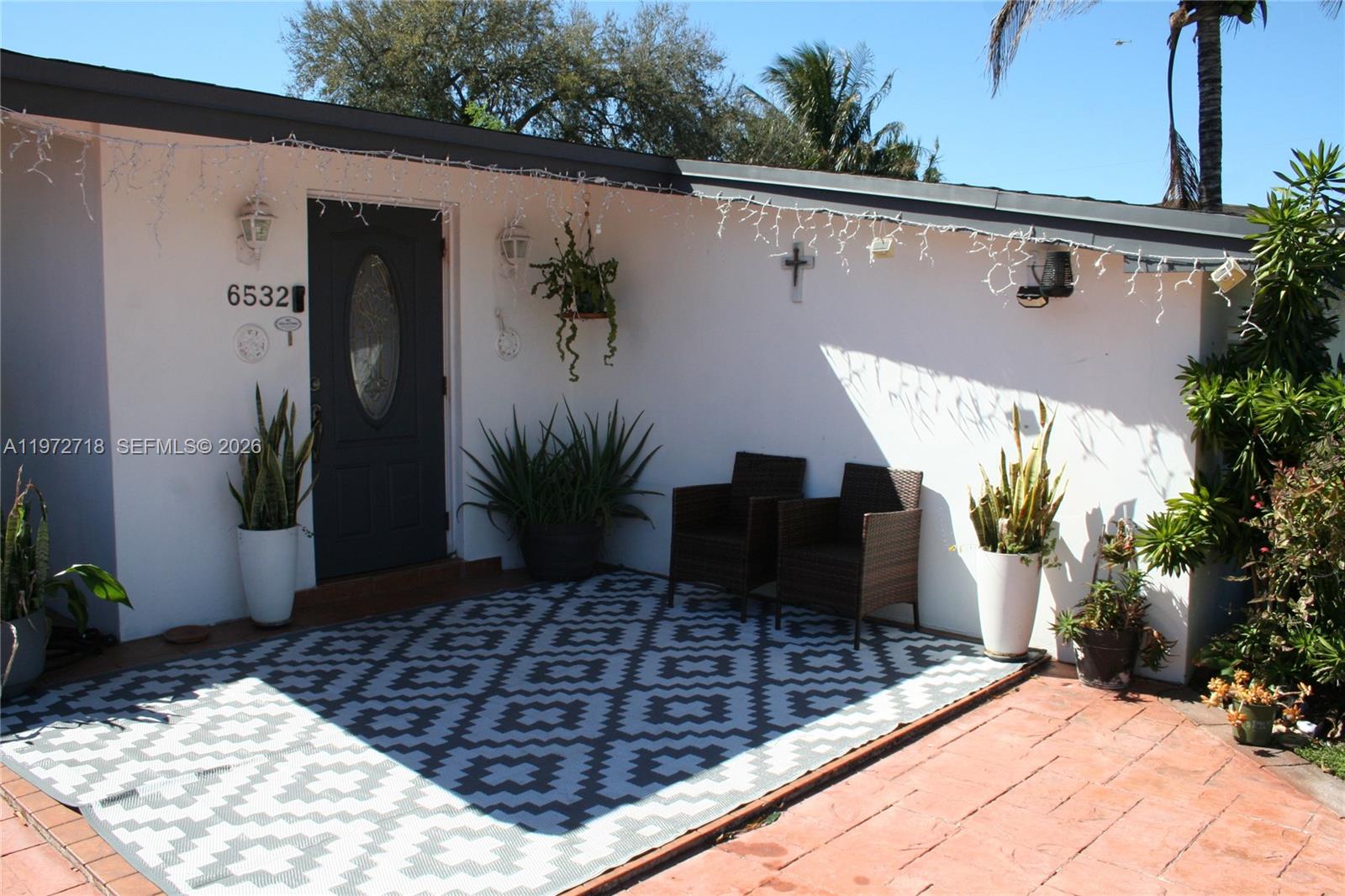 A patio area features a patterned rug, two wicker chairs, potted plants, and a doorway — 6532 Mayo St, Hollywood FL 33023, HOLLYWOOD, FL