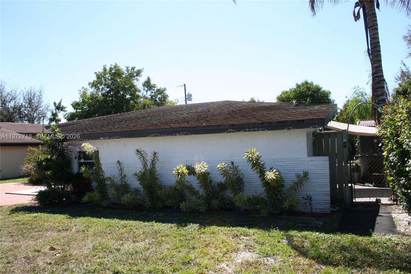 A white brick exterior wall of a house features a row of green plants — 6532 Mayo St, Hollywood FL 33023, HOLLYWOOD, FL