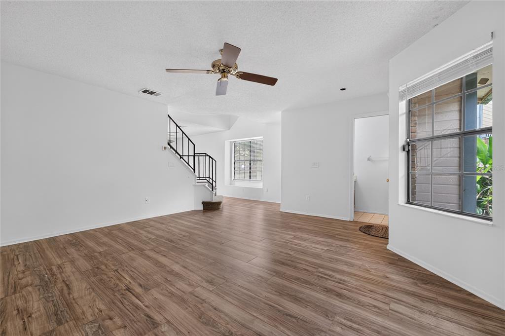 An empty living room features wood-look flooring, white walls, a ceiling fan, and a staircase — 2996 LOWELL COURT, CASSELBERRY, FL