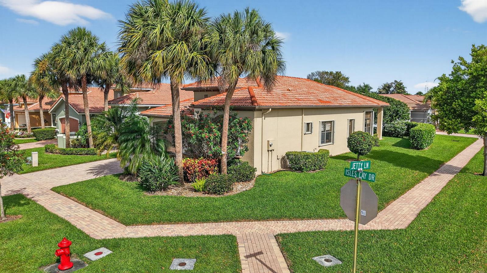 A beige house with a red tile roof sits on a corner lot with landscaping — 9571 Isles Cay Drive, Delray Beach FL 33446, DELRAY BEACH, FL