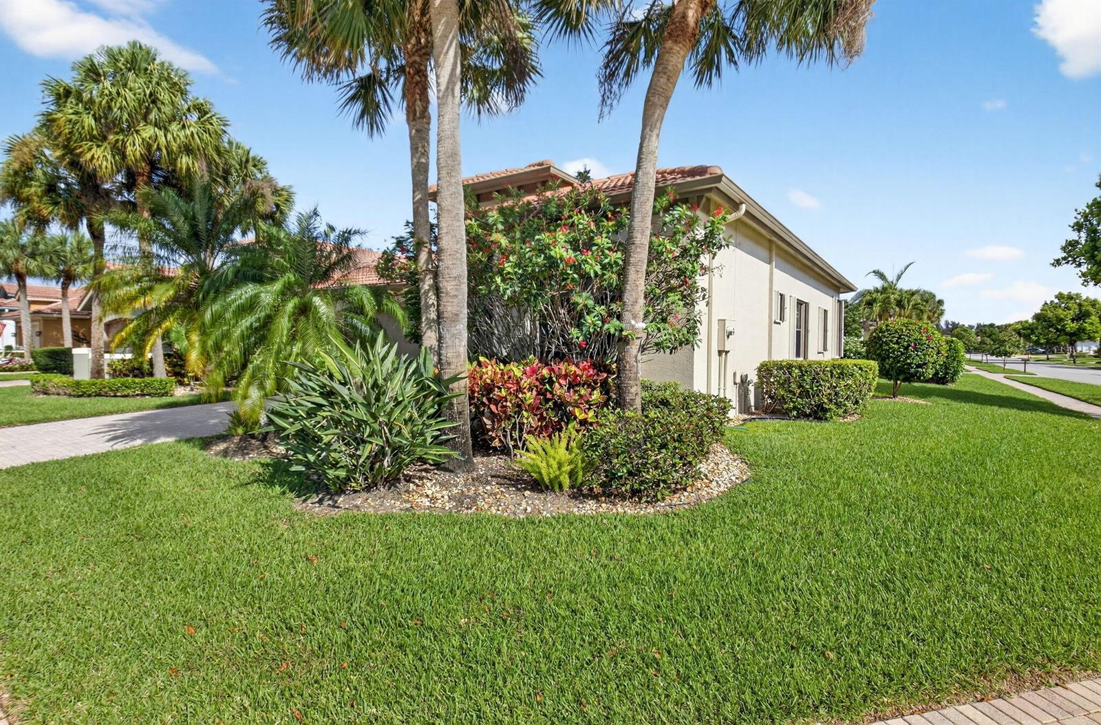 A side view of a house exterior featuring a landscaped garden with palm trees — 9571 Isles Cay Drive, Delray Beach FL 33446, DELRAY BEACH, FL