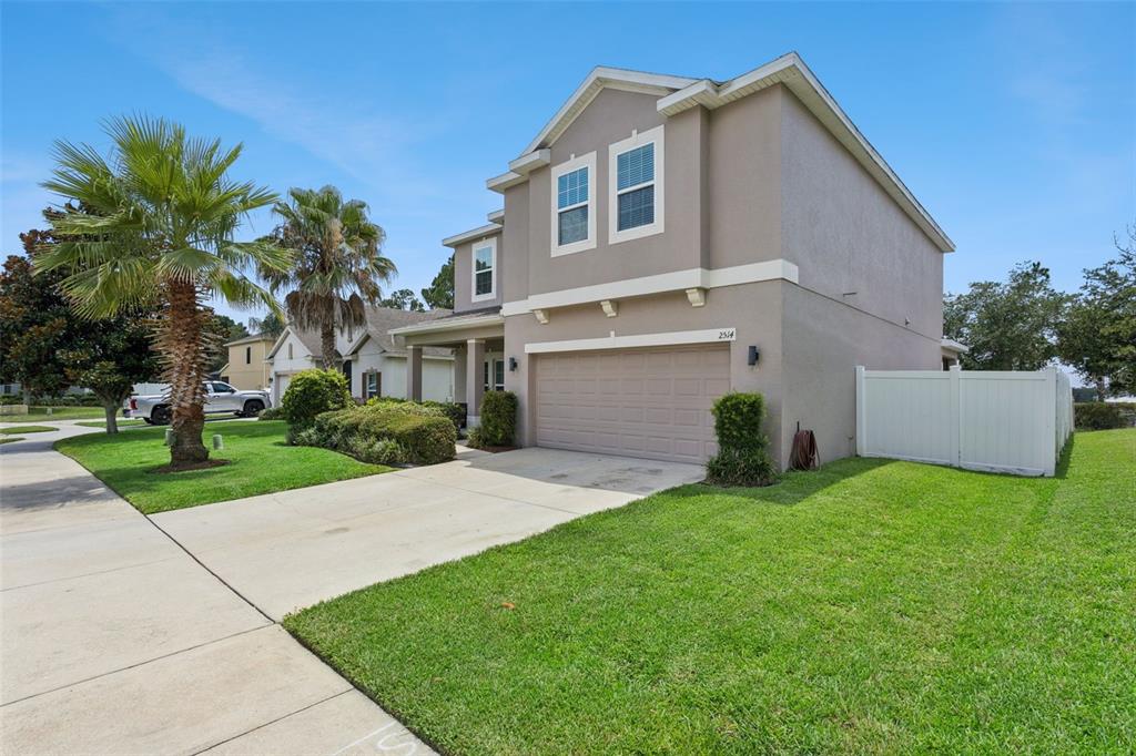 A two-story suburban house with a beige stucco exterior, a two-car garage, and a lawn — 2514 PLUMADORE DRIVE, GRAND ISLAND, FL