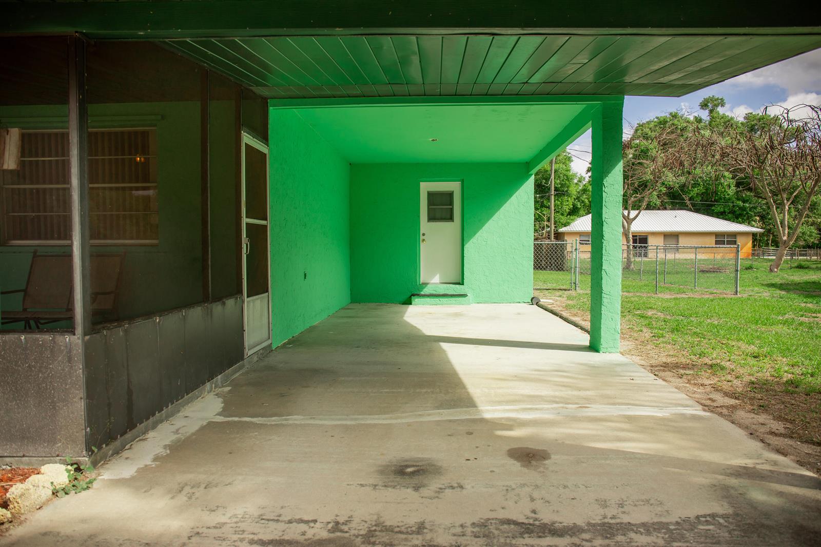 A bright green covered patio features a concrete floor and a white exterior door — 1120 SW 8th Court, Okeechobee FL 34974, OKEECHOBEE, FL