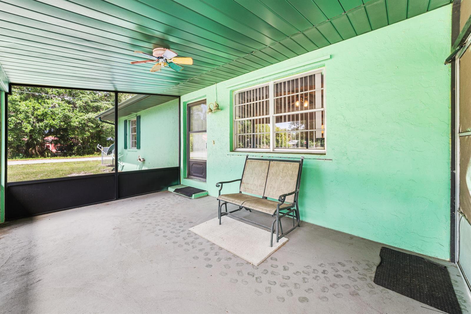 A screened-in porch features light green stucco walls, a green ceiling, and a metal bench — 1120 SW 8th Court, Okeechobee FL 34974, OKEECHOBEE, FL