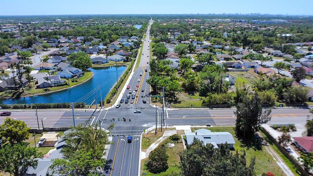 An aerial view shows a suburban intersection with a road, surrounding houses, and a pond — 7720 TUTTLE AVENUE, SARASOTA, FL