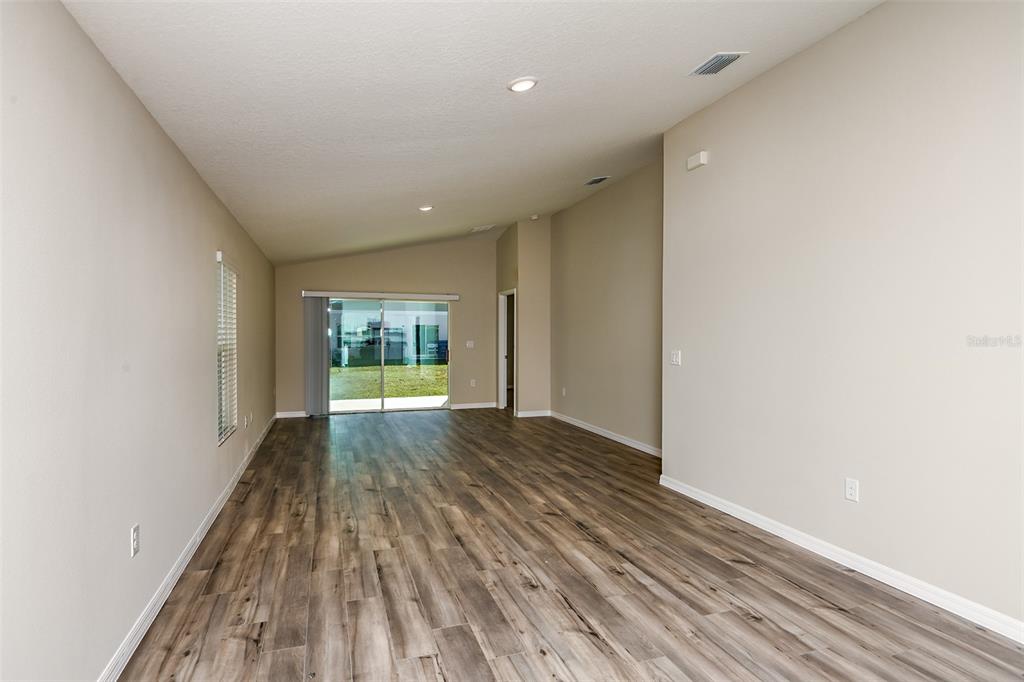An empty living room features light-colored walls, wood-look flooring, and a sliding glass door — 1585 SAGE AVENUE, HAINES CITY, FL