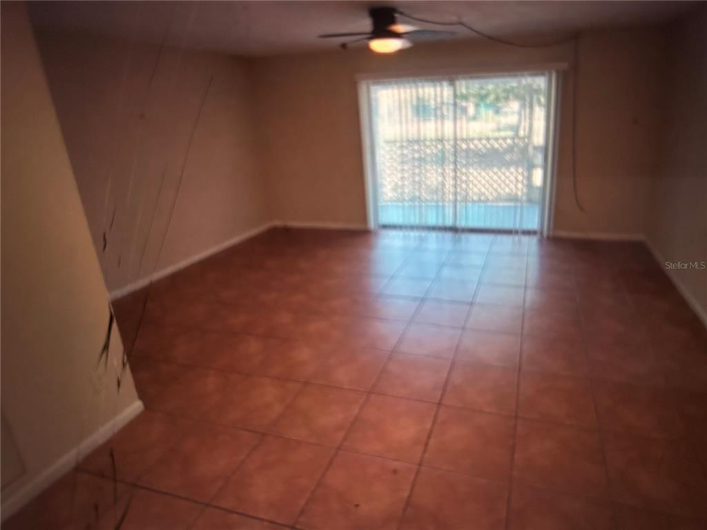 An empty room with brown tile flooring, a ceiling fan, and sliding glass doors — 3425 TRICON LANE UNIT 12, HOLIDAY, FL
